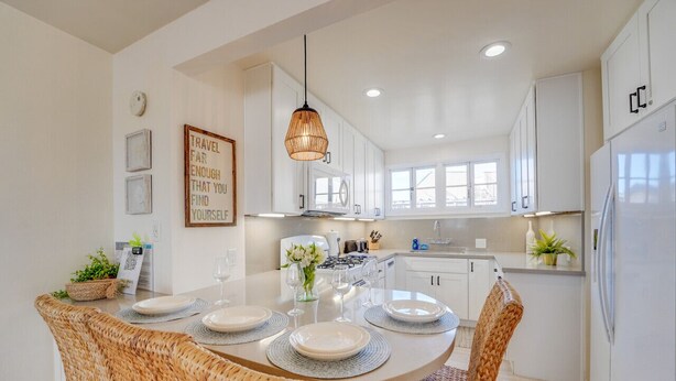 A modern kitchen with white cabinets, a central island with seating, and a hanging light fixture. - Driftwood Getaway! South Mission Beach (San Diego)