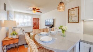 A modern living room with a dining area, a ceiling fan, a television, and a motivational quote on the wall. - Driftwood Getaway! South Mission Beach (San Diego)