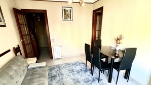 Un salon avec un canapé gris, une table à manger avec des chaises, un lustre et un tableau encadré au mur.