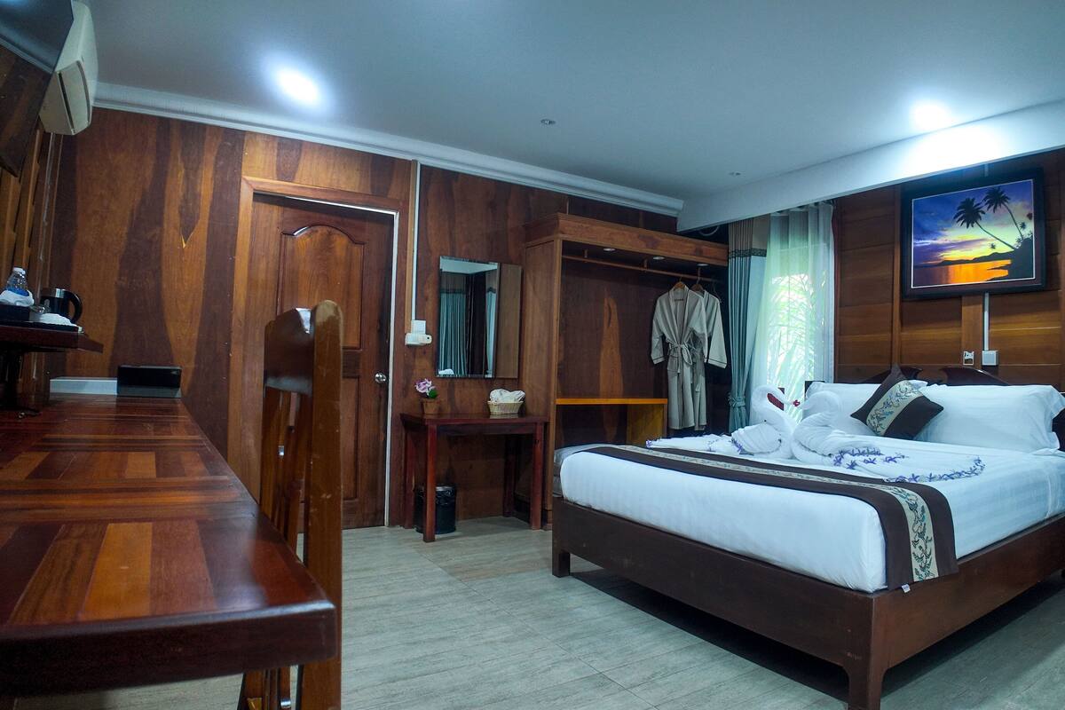 Una habitación de hotel con una cama de madera, un escritorio, un armario y un televisor en la pared.