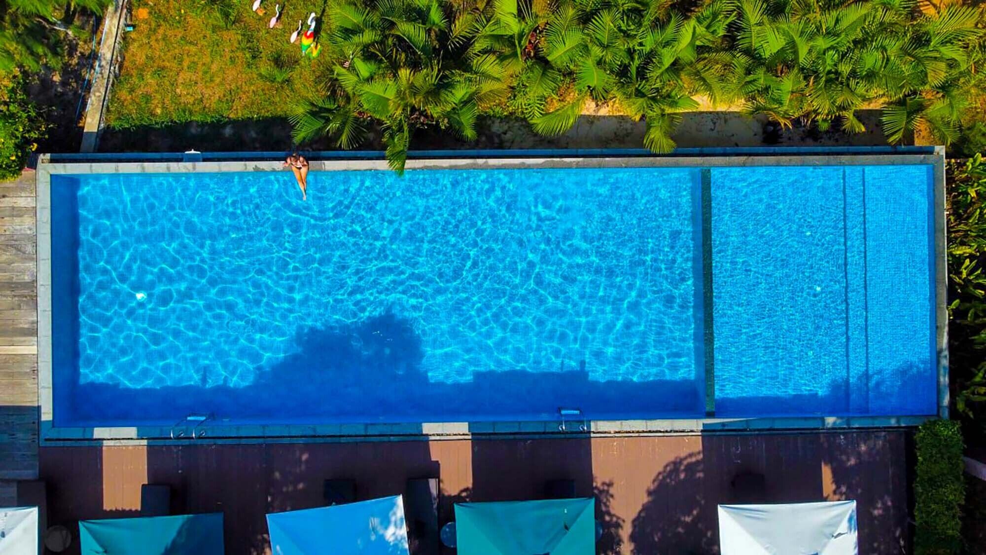 A rectangular swimming pool with clear blue water, surrounded by greenery and a wooden deck.