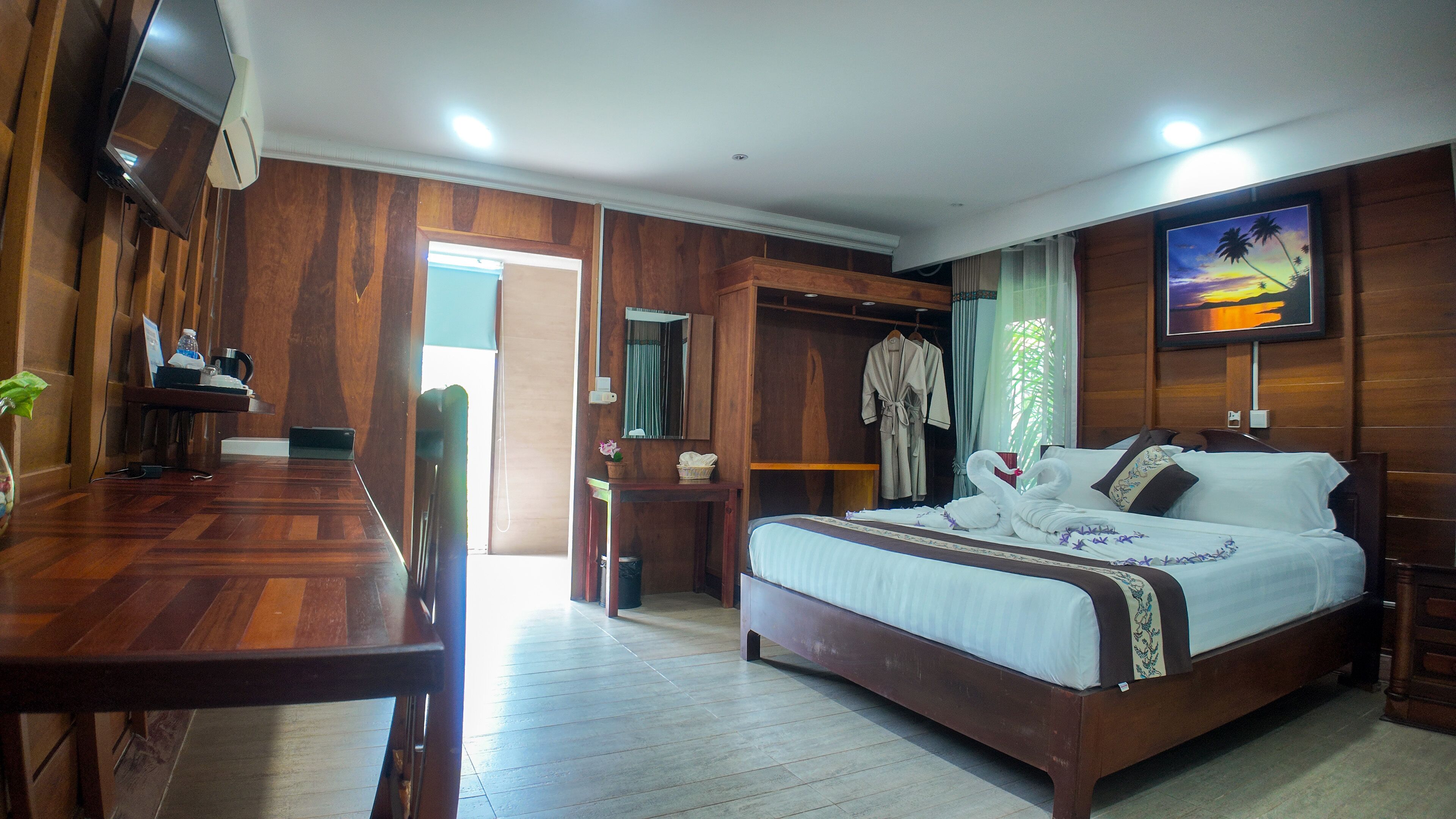 A hotel room with a wooden floor, a bed with white bedding, a TV on the wall, and a desk with a chair.