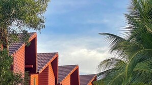 A row of red-roofed buildings with green windows, surrounded by palm trees and a paved walkway. - Lodge Moni Essara Kompot (Kampot)