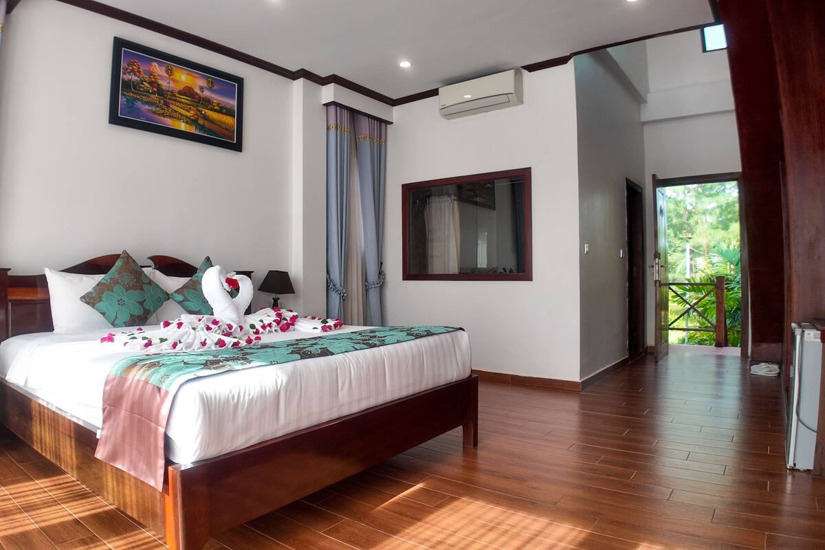 Un dormitorio espacioso con una cama de madera, un cuadro y vistas al verdor exterior.