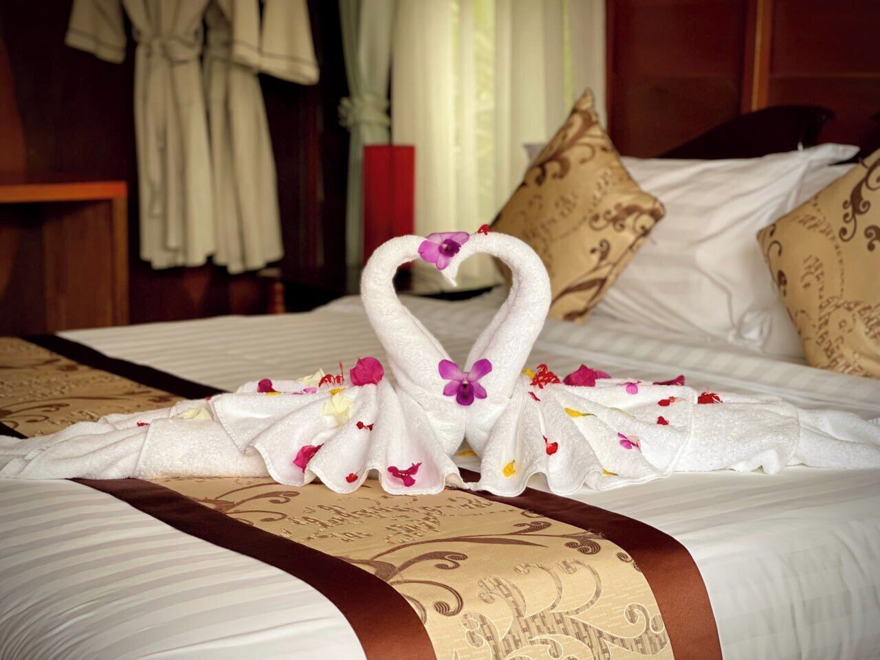 A neatly made bed with a towel arranged in the shape of a swan, adorned with flowers, in a hotel room with patterned bedding and pillows.