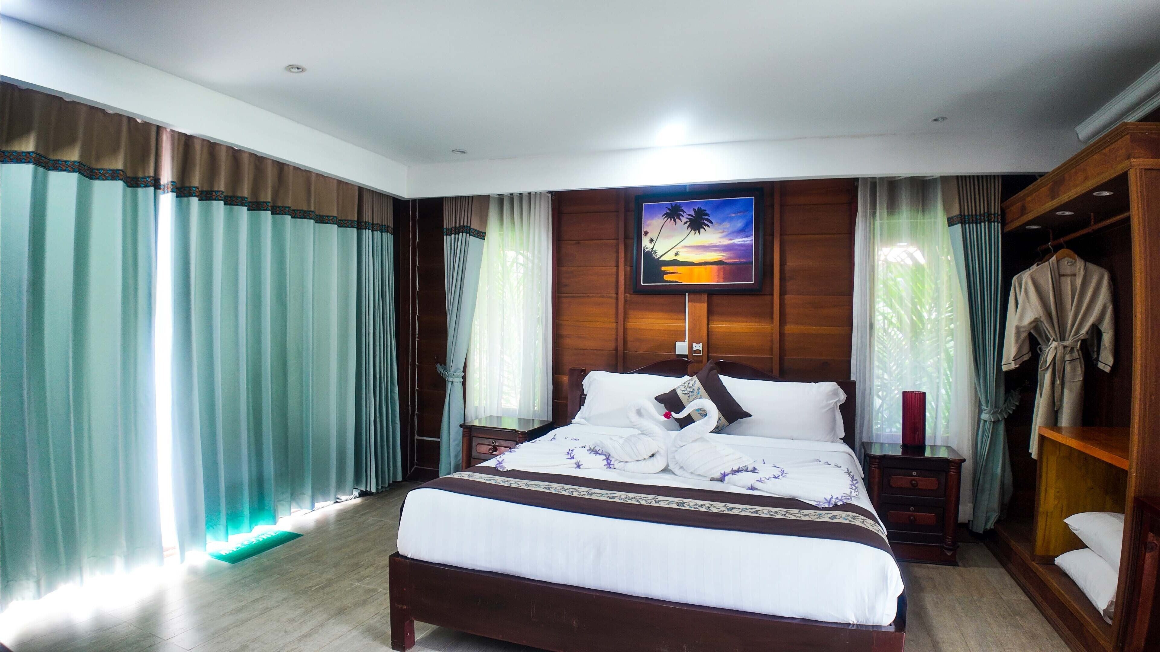 A hotel room with a large bed, wooden paneling, a painting of a sunset, and a robe hanging on the door.