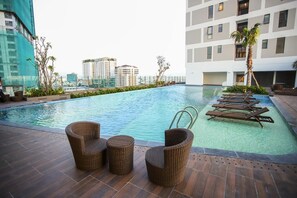 A rooftop pool with wicker chairs and lounge areas, surrounded by buildings and palm trees. - RIVERGATE apartment infinity pool & Gym  (Ho Chi Minh City)