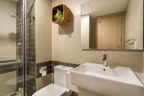 A modern bathroom with a glass shower enclosure, a white sink, and a wooden plant shelf. - RIVERGATE apartment infinity pool & Gym  (Ho Chi Minh City)