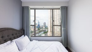 A hotel room with a large bed, grey curtains, and a view of a cityscape through a large window. - RIVERGATE apartment infinity pool & Gym  (Ho Chi Minh City)