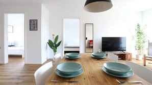 A modern dining area with a wooden table, teal plates, and white chairs. - Apartment "London" 63m² |Cologne|Messe|Phantasialand|Bonn (Erftstadt)