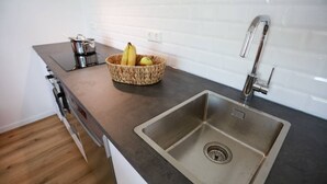 A kitchen with a stainless steel sink, a basket of fruit, and a pot on the countertop. - Apartment "London" 63m² |Cologne|Messe|Phantasialand|Bonn (Erftstadt)