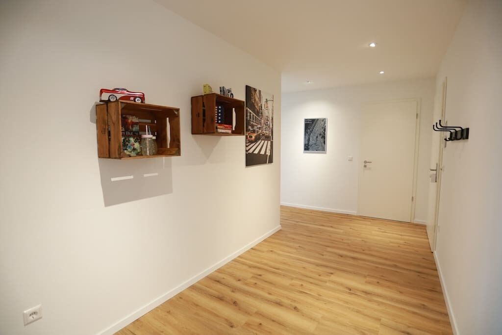 Een gang met houten vloeren, witte muren en kunstwerken aan de wanden.