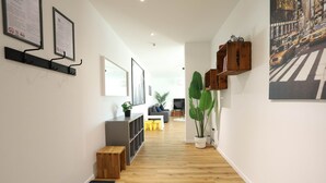 A hallway with wooden flooring, a grey sofa, a coffee table, and a large green plant.