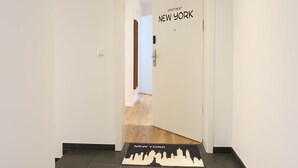 A hallway with a door labeled "Apartment New York" and a cityscape mat on the floor.