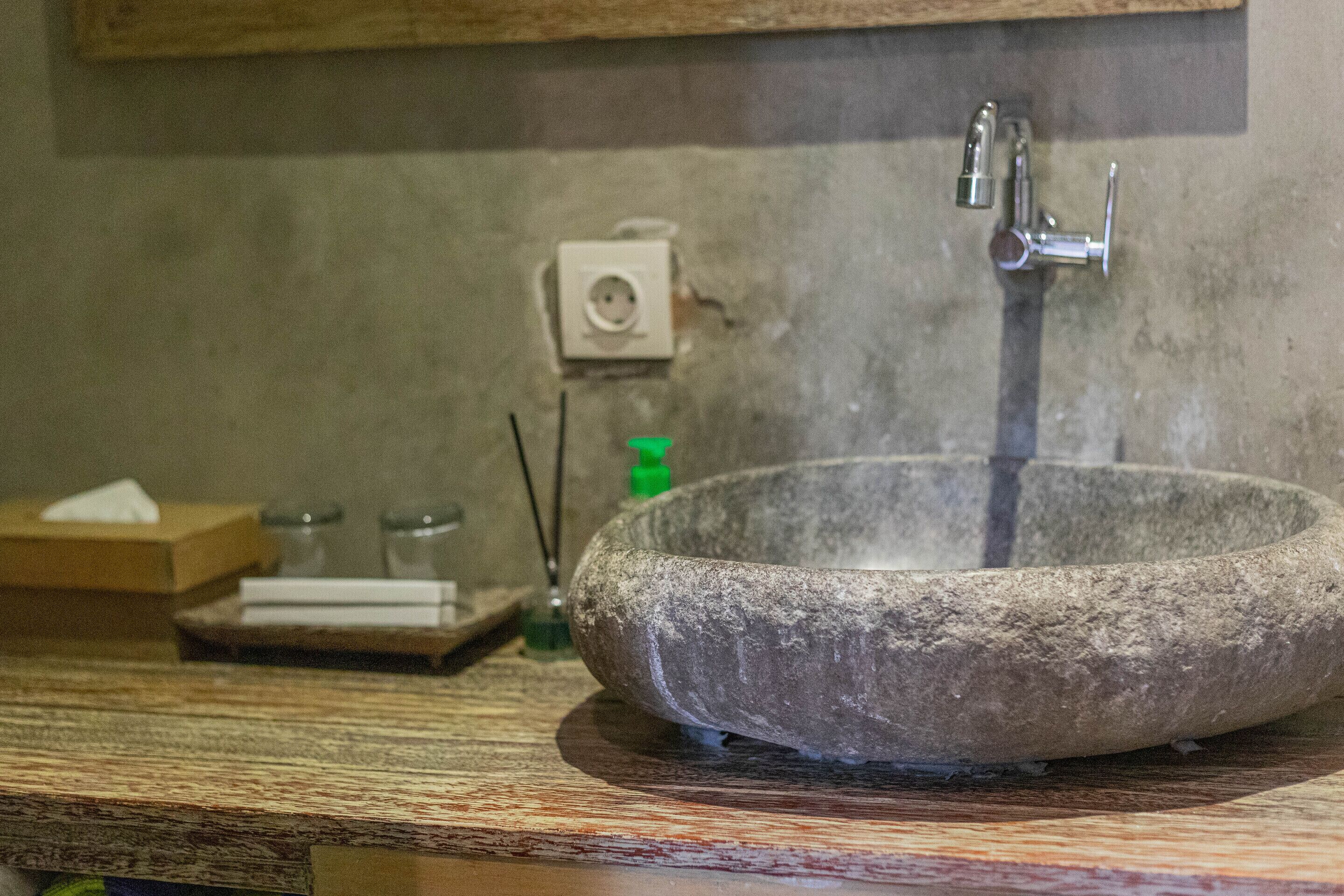 A stone sink with a faucet, a wooden countertop, and a small box with tissues.