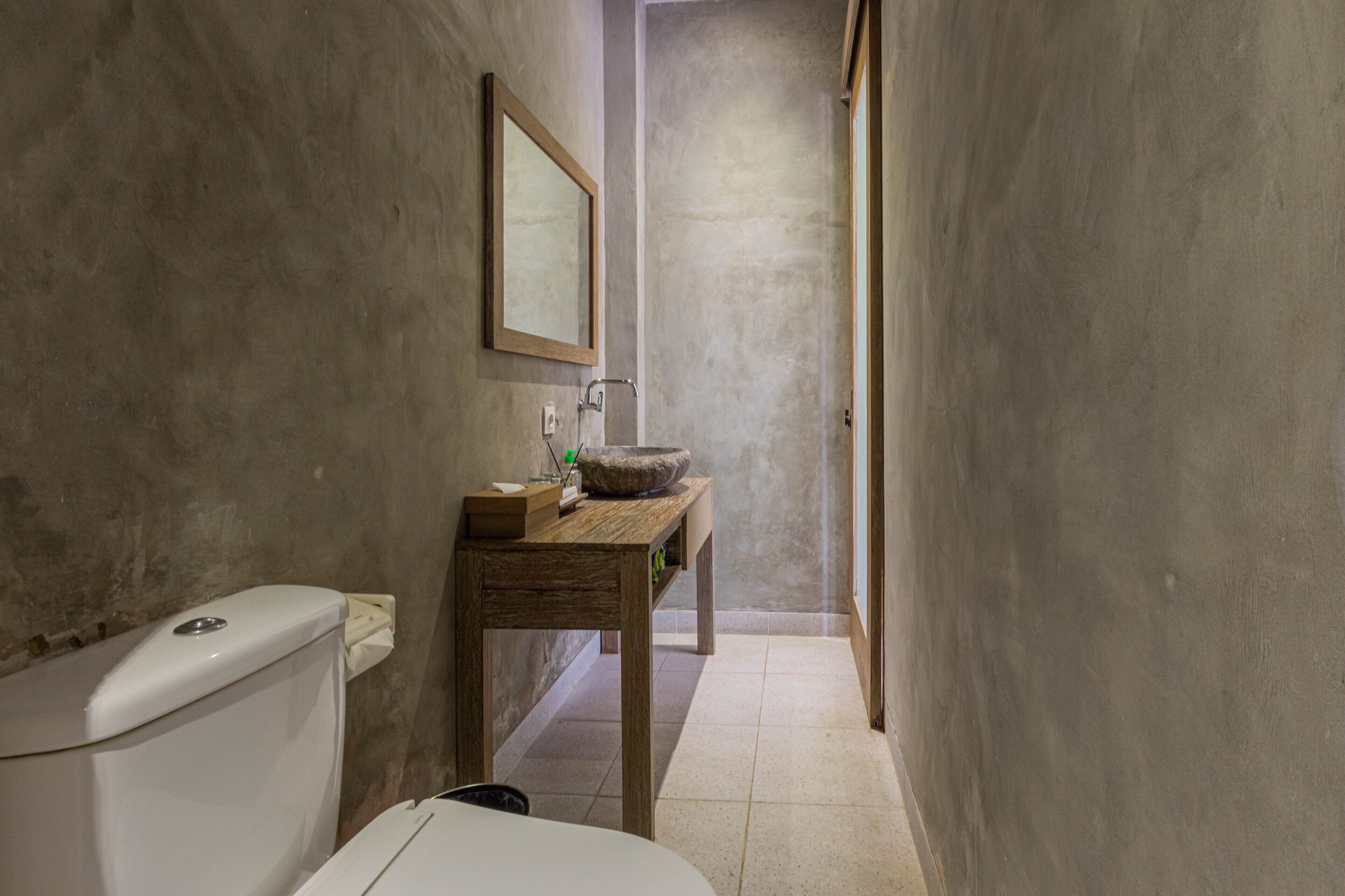 A narrow bathroom with a wooden vanity, a large mirror, and a stone sink.