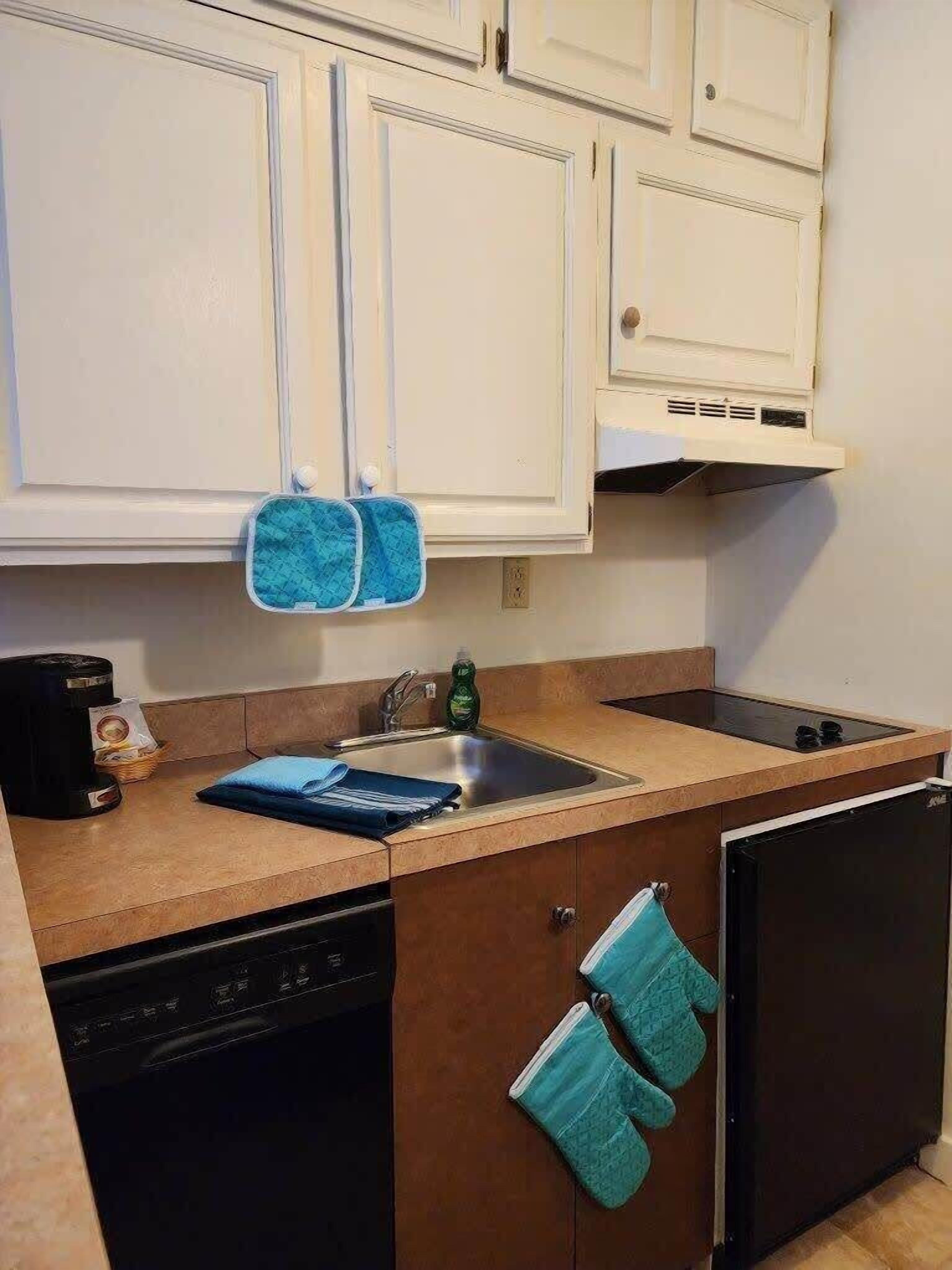 Una cocina compacta con armarios blancos, un lavamanos, lavavajillas y refrigerador.
