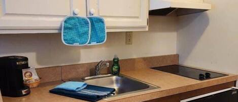 Una cocina compacta con armarios blancos, un lavamanos, lavavajillas y refrigerador.