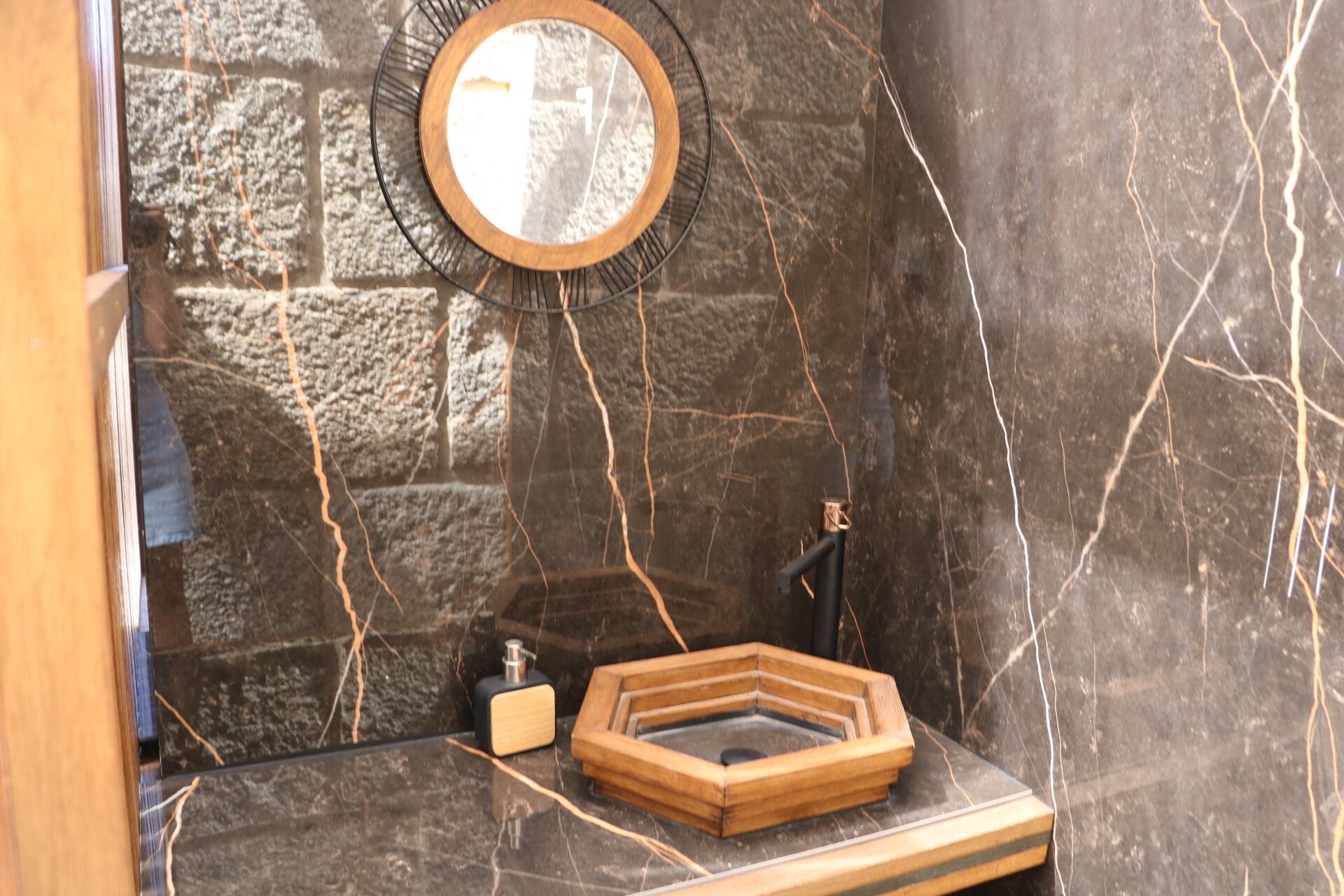 A bathroom with a stone wall, a wooden vanity, a mirror, and a sink.