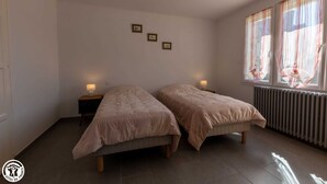 A bedroom with two beds, a radiator, and a window with curtains. - La Maison de Fabrice (Vauchamps)