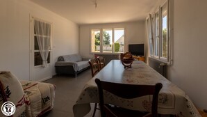 A dining area with a table set for four, a sofa, and a TV. - La Maison de Fabrice (Vauchamps)