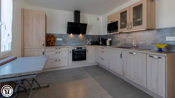 A modern kitchen with light wood cabinets, a built-in oven, a microwave, and a sink. - La Maison de Fabrice (Vauchamps)