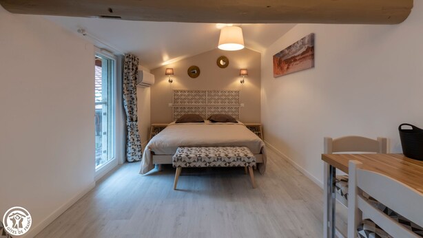 Un dormitorio con cama, lámparas de noche, una ventana con cortinas y una viga de techo de madera.