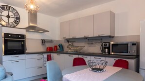 Una cocina moderna con armarios blancos, horno empotrado, microondas y un comedor con mesa y sillas.