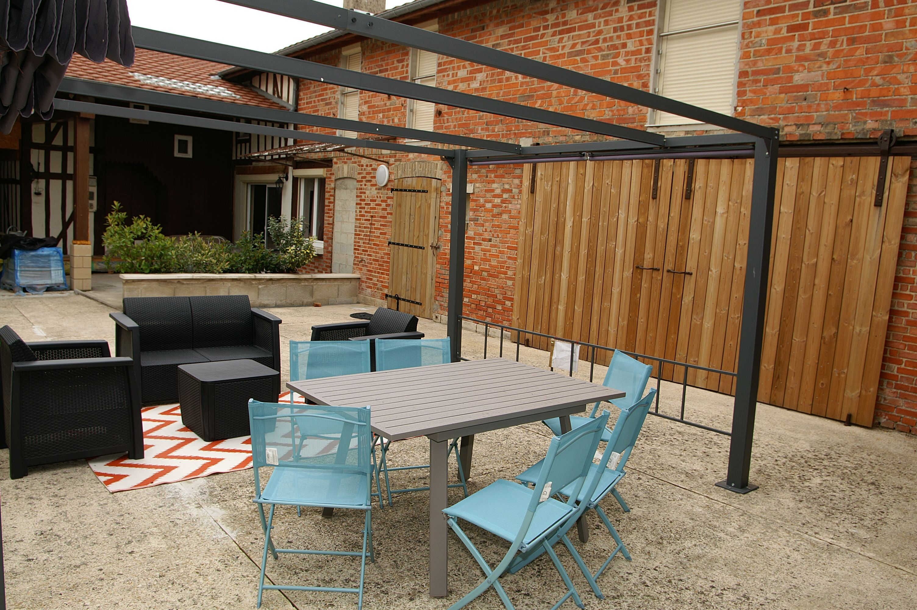 En uteplats med en pergola av metall, ett bord och blå stolar.