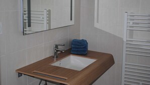 Une salle de bain avec un meuble-lavabo en bois, un lavabo blanc, un miroir et un porte-serviettes.
