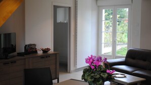 Un salon comprenant un canapé, une table à manger avec des chaises, un téléviseur et une fenêtre donnant sur un paysage verdoyant.
