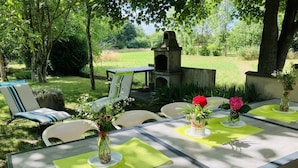 An outdoor dining area with a long table, chairs, and a stone oven in the background. - Les Trelles - Pleurs (Pleurs)