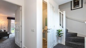 Un pasillo con una escalera que sube a un segundo piso, una puerta de acceso a un baño y una sala de estar con un sofá y una lámpara.