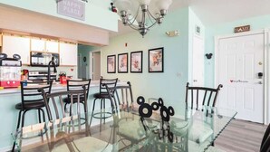 A dining area with a glass table surrounded by chairs, a kitchen in the background, and a door labeled "HOME". - Disney, Pool, Hot Tub, Gym! (Kissimmee)