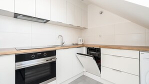A compact kitchen with white cabinetry, a built-in oven, a dishwasher, and a wooden countertop. - Tasteful Apartment in Poznan | Private Parking (Poznan)