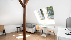 A modern, well-lit room with a wooden ceiling, a grey sofa, a round table, and a white desk with a computer. - Tasteful Apartment in Poznan | Private Parking (Poznan)