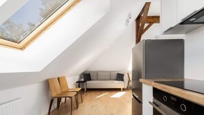 A modern loft-style room with a skylight, a sofa, a dining area, and a kitchenette. - Tasteful Apartment in Poznan | Private Parking (Poznan)