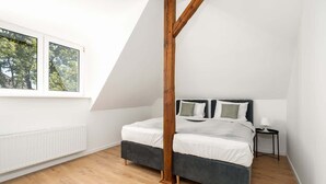 A bedroom with a sloped ceiling, a bed with dark grey bedding, a wooden post, a small bedside table, and a window with a view of trees. - Tasteful Apartment in Poznan | Private Parking (Poznan)
