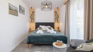 A modern bedroom with a large bed, a side table, a chair, and a view of the outdoors.