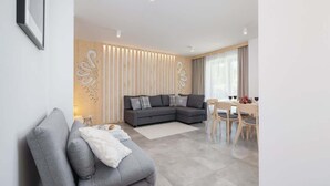 A modern living room with a grey sofa, a dining table with chairs, and a decorative wall panel.