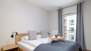 Une chambre moderne avec un lit en bois, une literie grise, une table de chevet avec une lampe et une fenêtre avec des rideaux.
