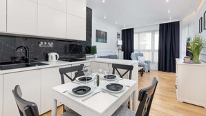 Una cocina moderna con armarios blancos, encimera negra y zona de comedor con mesa blanca para cuatro.