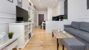 Una sala de estar moderna con un sofá gris, una mesa de centro de madera y un televisor sobre un mueble blanco.