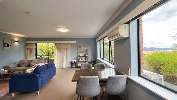 Un salon moderne comprenant un canapé, une table à manger et des chaises, une fenêtre avec vue et un appareil de climatisation.