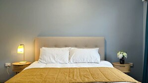 Un lit avec une tête de lit blanche, un plaid jaune et une lampe de chevet.