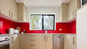 Une cuisine avec des meubles blancs, un mur d’accent rouge, une fenêtre et un lave-vaisselle.