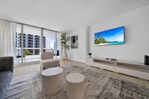 A modern living room with a large window, a flat-screen TV, a sofa, and a coffee table. - King bed and balcony near Art Miami | Pool access (Miami)