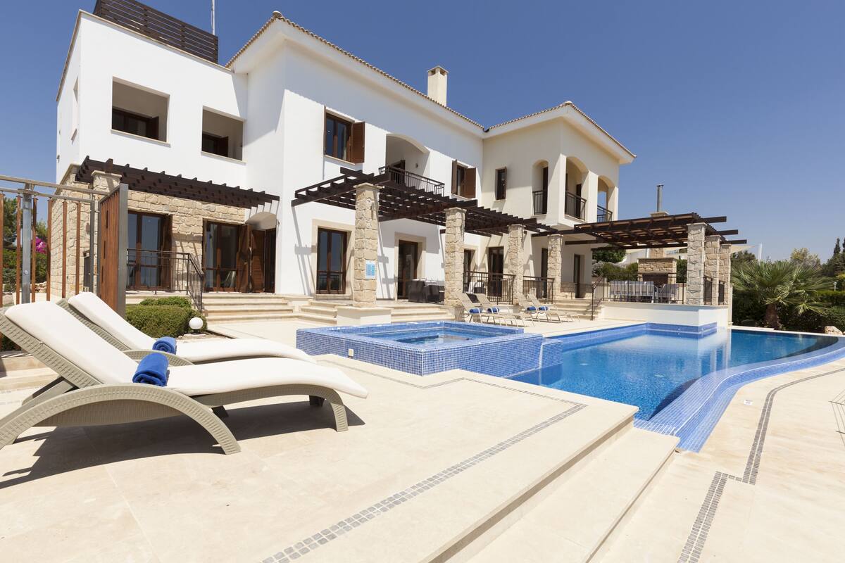 A modern villa with a swimming pool, lounge chairs, and a pergola.