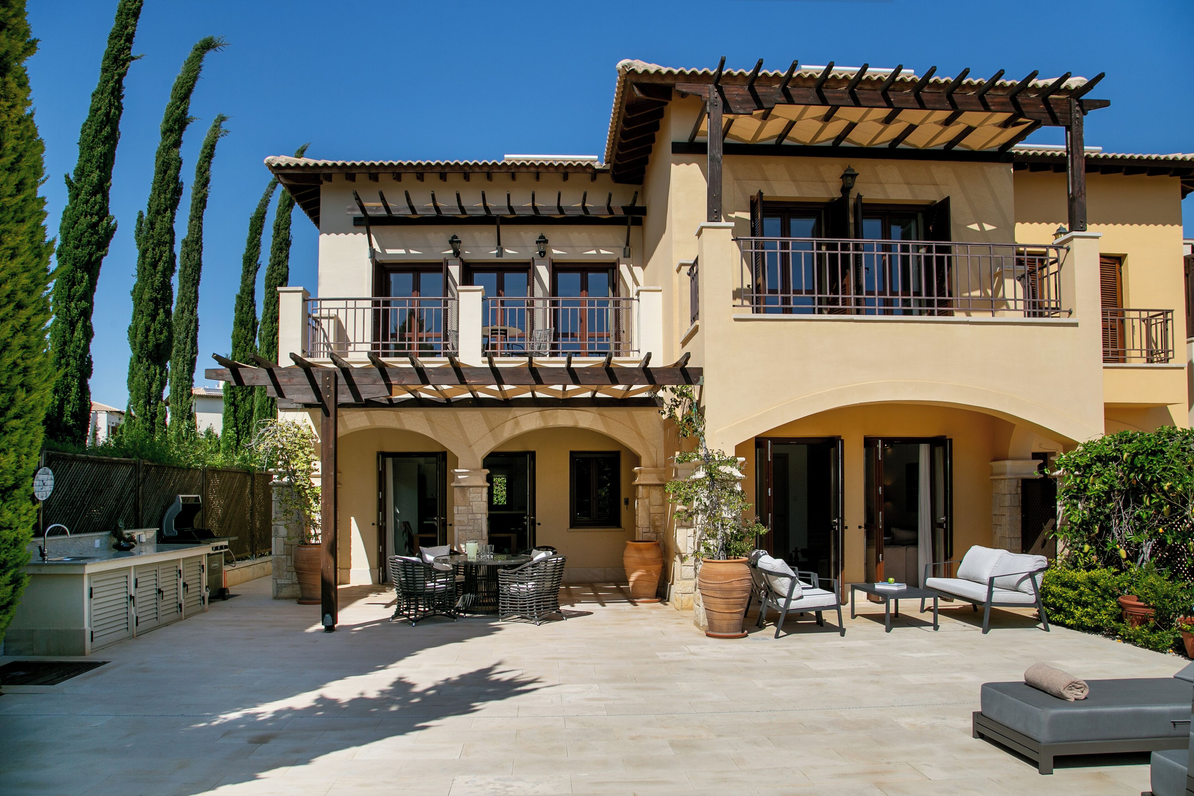 Ein zweigeschossiges Haus mit einer Terrasse, die Gartenmöbel und einen Grill beinhaltet.