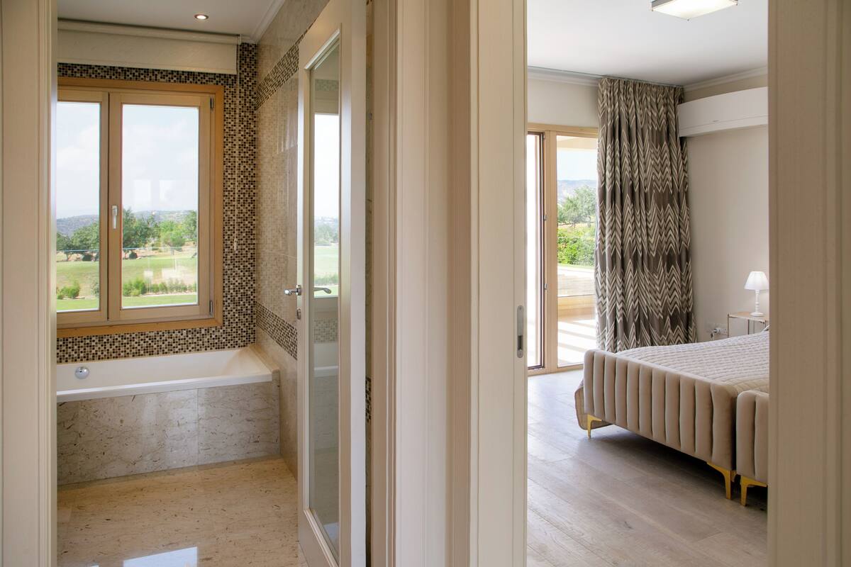 A bedroom with a large bed, a bathroom with a bathtub, and a view of the outdoors.